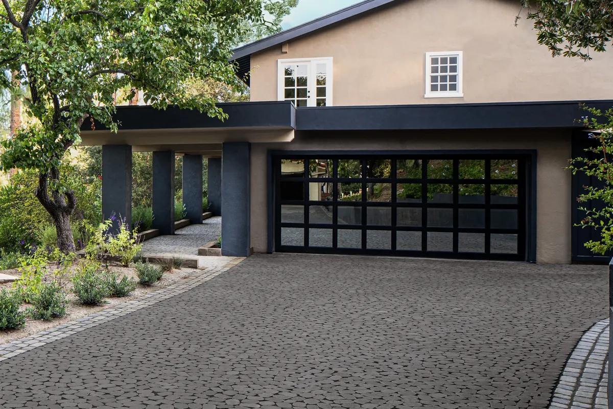 A wide paver driveway with a stone-set border leading to a garage, with a planted side path